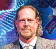 This is an image of University of Cambridge professor Giles Oldroyd. He is smiling and wearing a tweed suit. He is in front of a backgroud consisting of science related materials like DNA and a microscope