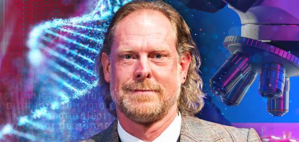 This is an image of University of Cambridge professor Giles Oldroyd. He is smiling and wearing a tweed suit. He is in front of a backgroud consisting of science related materials like DNA and a microscope