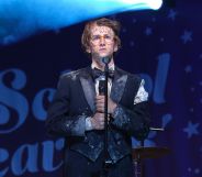 Sebastian Croft wears a filthy suit while standing on a stage and holding a microphone in a new still from new film How To Date Billy Walsh.