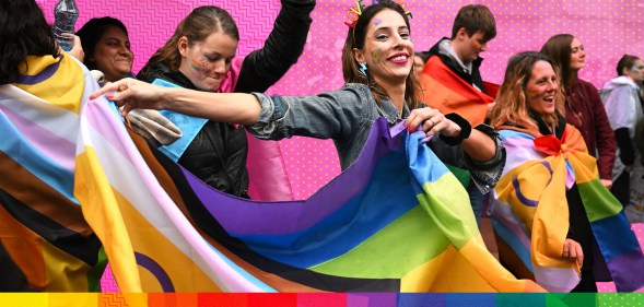 People marching in Pride, holding Progress Pride flags