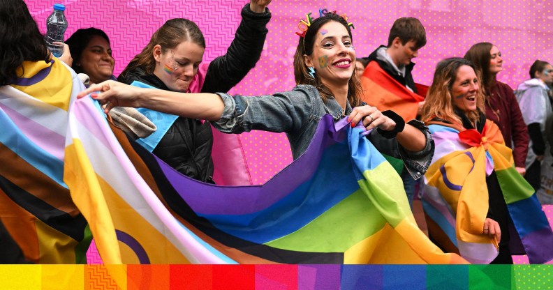 People marching in Pride, holding Progress Pride flags