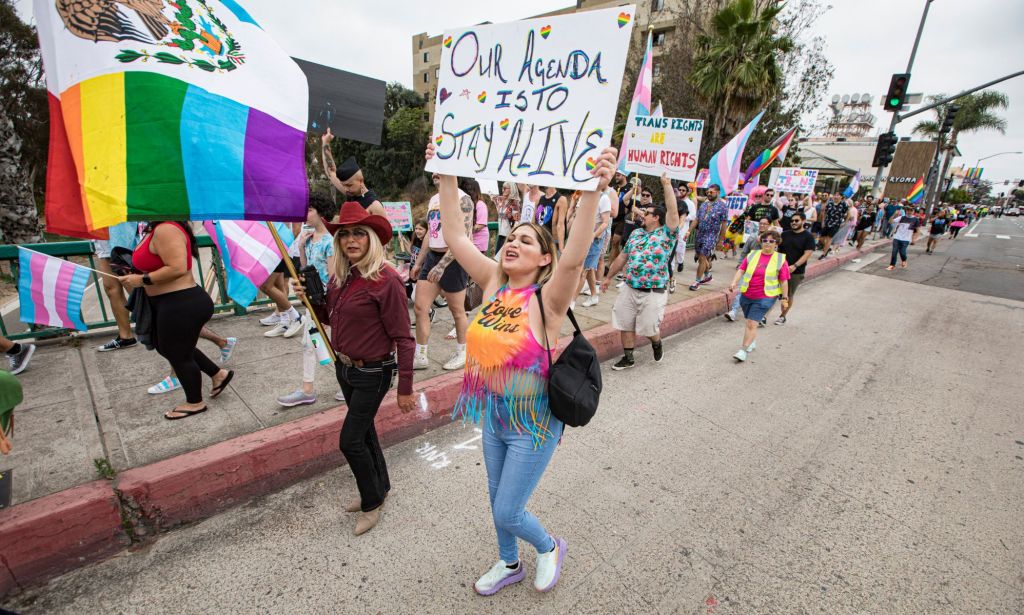 A person holds up a sign reading 'our agenda is to stay alive' as another person holds up an LGBTQ+ flag during a LGBTQ+ and trans Pride protest against Republican and conservative hate