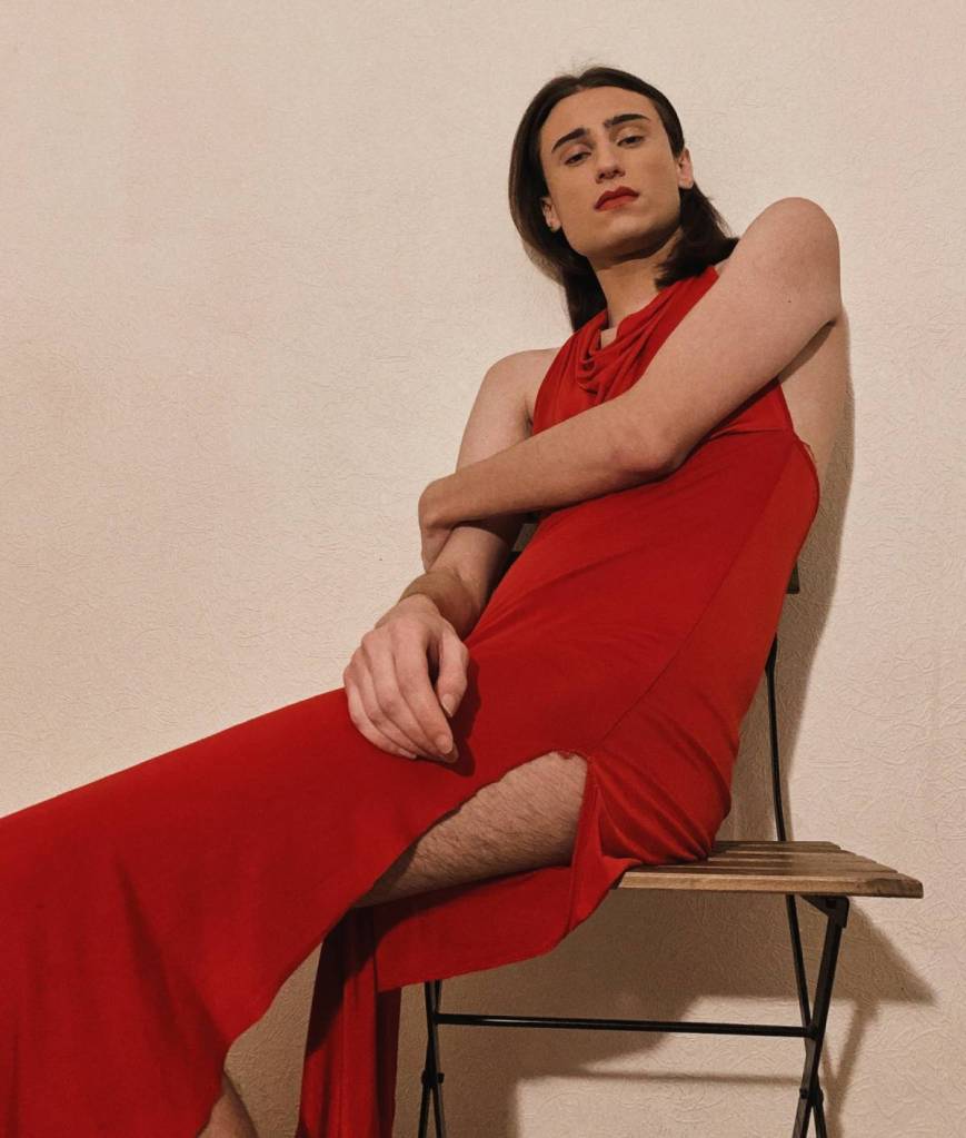 Mihelina, a Georgian trans woman living in Russia, has long dark brown hair and is wearing a red dress as she sits posed on a chair