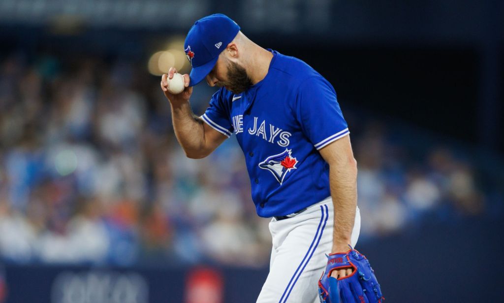 Toronto Blue Jays pitcher Anthony Bass wears a blue baseball uniform and matching cap with white trousers as holds his cap and a ball with one hand during a game