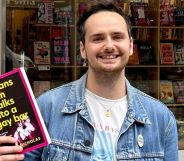 A picture of Harry Nicholas, in a denim jacket, holding a book that reads "A Trans Man Walks into a Gay Bar."