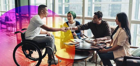 This is an image of a man in a wheelchair shaking another mans hand. There are two women smiling. They are in a bright and airy office.