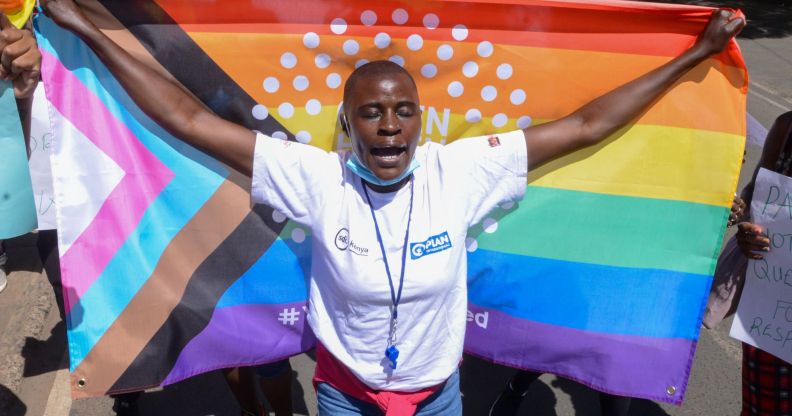 A Kenya LGBTQ+ activist holds up a Progress Pride flag behind them.