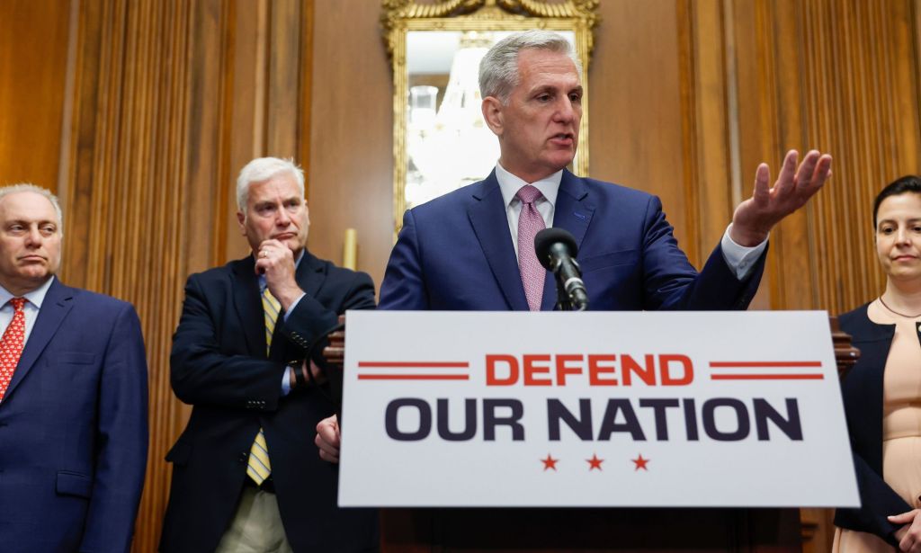 (L-R) Steve Scalise, Tom Emmer, Kevin McCarthy and Elise Stefanik stand around a press room discussing the recently passed National Defense bill, with McCarthy at a podium that says "defend our nation."