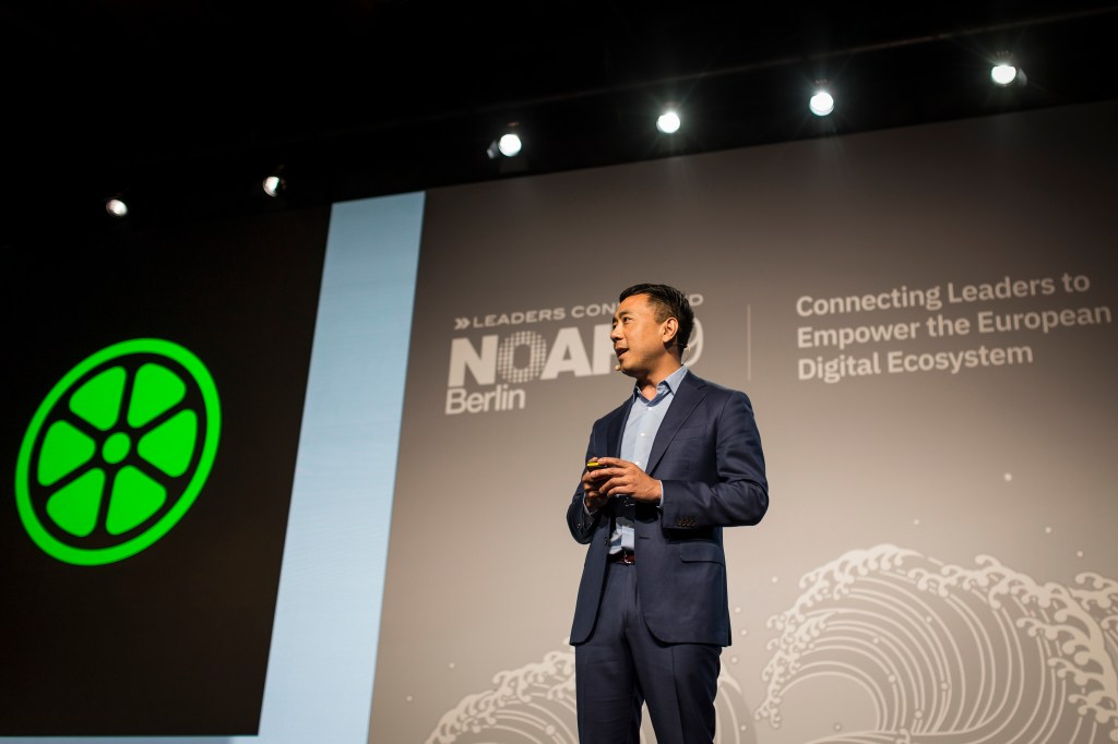 This is an image of Lime CEO Wayne Ting speaking on stage at a conference. He is looking off and is wearing a dark blue suit.