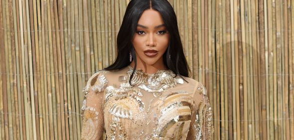 Munroe Bergdorf in a gold dress, stood against a gold background.