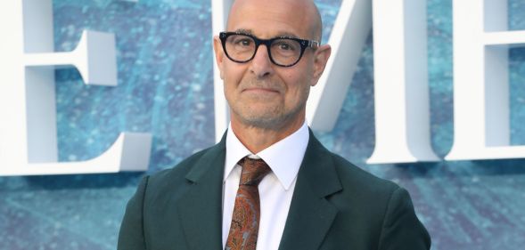 Stanley Tucci at the UK premiere of The Little Mermaid, wearing a green suit and red tie with black rimmed glasses.