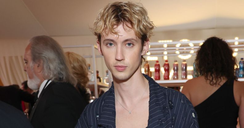 Troye Sivan wears a black pinstriped blazer and low cut top.