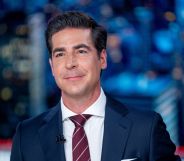 Fox News host Jesse Watters wears a suit and tie and sits at a desk