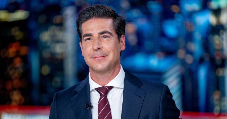 Fox News host Jesse Watters wears a suit and tie and sits at a desk