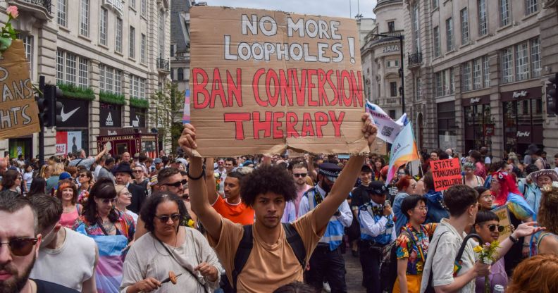 Protester in crowd holds up a sign that reads "No more loopholes! Ban conversion therapy!"