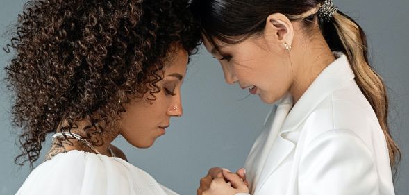 A queer, same-sex couple wear white outfits as they attend a wedding and hold each other's hands