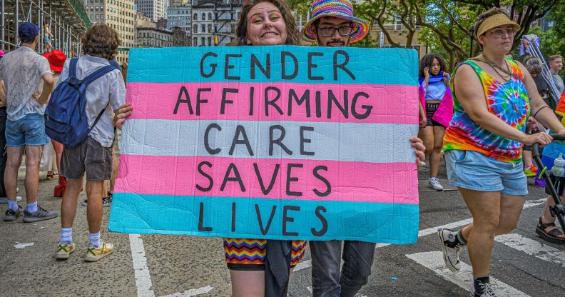 A person holds up a sign during an LGBTQ+ demonstration that reads 'gender-affirming care saves lives' in the colours of the trans pride flag