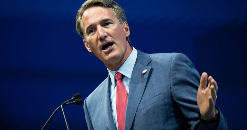 Virginia governor Glenn Youngkin wears a blue shirt, red tie and blue suit jacket as he gestures with one hand raised while standing at a podium