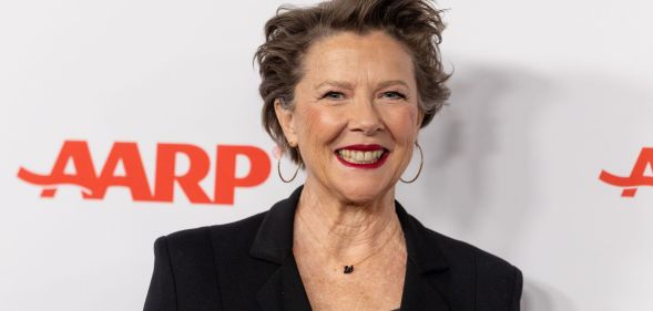 Annette Bening in a black blazer and top smiling at the camera while on the red carpet.