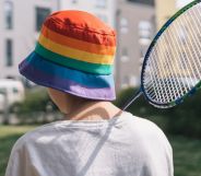 A person with a rainbow bucket hat holds a badminton racket.