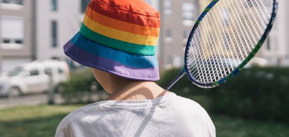 A person with a rainbow bucket hat holds a badminton racket.