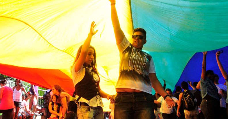 Crowds celebrate during a Brazil Pride march under a giant LGBTQ+ flag.