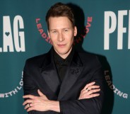 Dustin Lance Black poses on the red carpet in a black suit and shirt