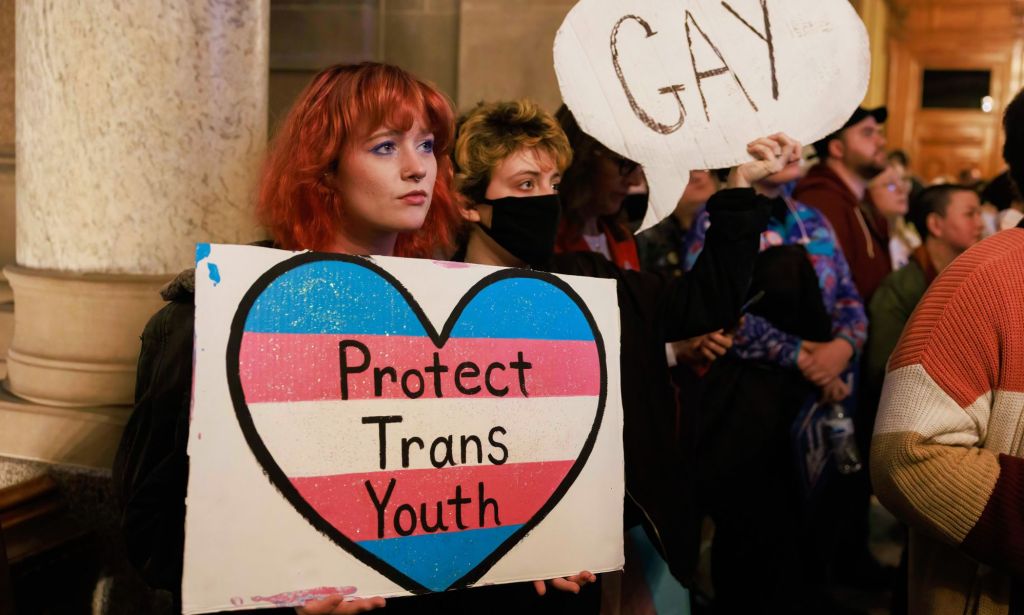 A protestor holds up a card reading "protect trans youth"