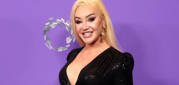 Kylie Sonique Love wears a black dress to an LGBT Gala in 2023. She is smiling at the camera and standing against a purple background.