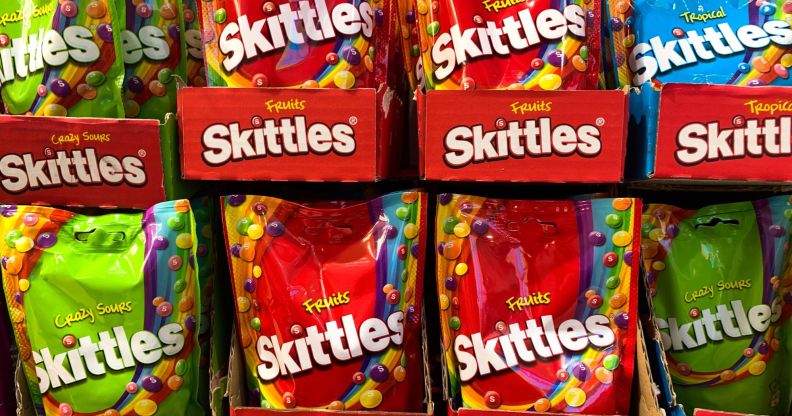 A set of Skittles packets in a supermarket, both red and green packets are on display.