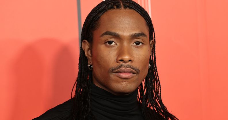 Steve Lacy in a high-necked black top, stood against an orange background.