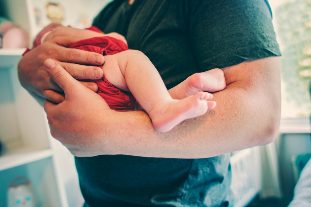 This image shows a father holding his baby. The image only shows his torso and the baby's face is also obscured. 