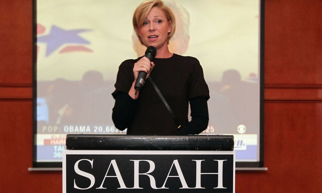 Former Texas state representative Sarah Davis, a Republican, stands at a podium while speaking into a microphone. Davis was a GOP politician who spoke out against anti-abortion, anti-trans, anti-LGBTQ+ policies within her party