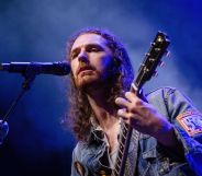 Singer Hozier wears a denim top as he plays a guitar and sings into a microphone