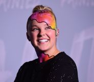 JoJo Siwa wears a black top as she poses with rainbow makeup on her head and neck