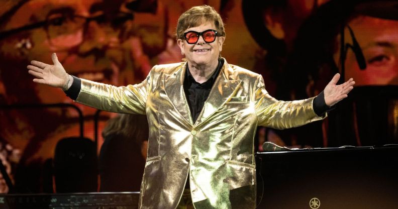 Elton John stands on stage wearing a gold suit