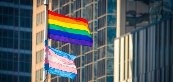 Rainbow flag and Trans flag on a flagpole in front of office buildings