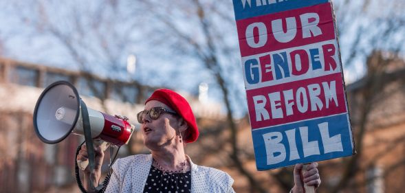 Activist Sarah Jane Baker holds a sign reading "where's our gender reform bill?" and speaks into a bullhorn