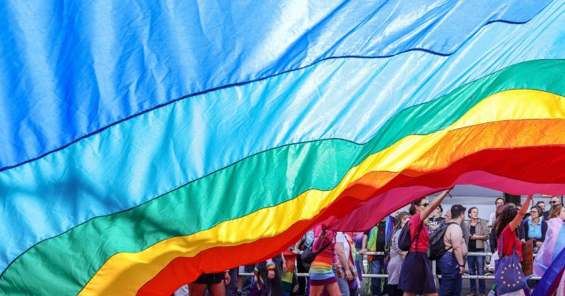 An LGBTQ+ flag draped over protestors.