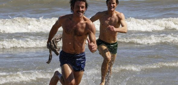 Jonathan Bailey and Matt Bailey chase each other on a beach in a still from Fellow Travelers.