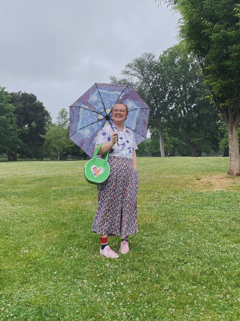 Ash Jayy pictured outdoors holding an umbrella on a cloudy day.