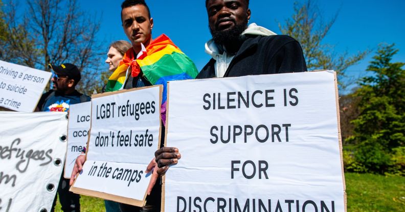 People hold up signs bringing awareness to the plight of LGBTQ+ people seeking asylum abroad including a sign reading 'silence is support for discrimination' and another reading 'LGBT refugees don't feel safe in the camps'