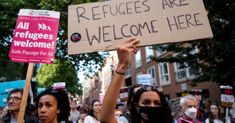 This image shows demonstrators taking part in a protest in favour of refugees. One in the middle is holding up a sign that says "refugees welcome here".