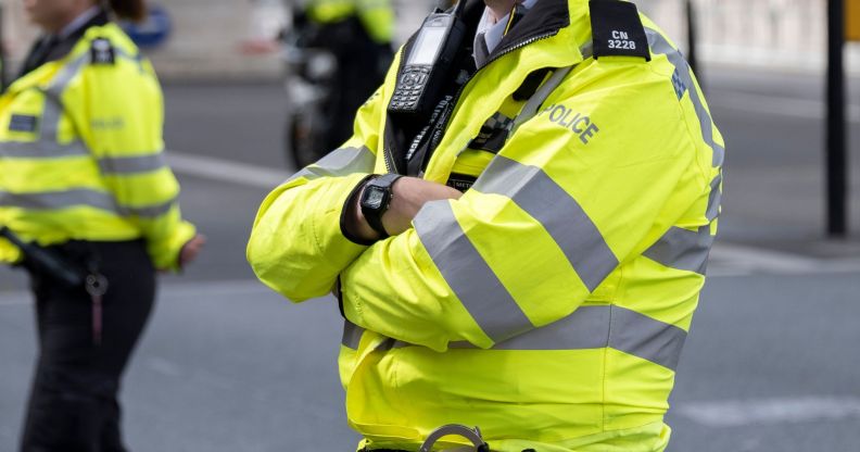 A male Metropolitan Police officer wears yellow reflective gear as he crosses his arms.