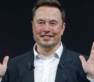 Elon Musk smiles with his hands raised.