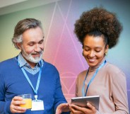 This is an image of two people looking at an iPad, the man on the left is wearing blue. The woman on the right is Black and is wearing a pinkish jumper.