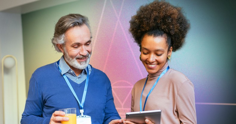 This is an image of two people looking at an iPad, the man on the left is wearing blue. The woman on the right is Black and is wearing a pinkish jumper.