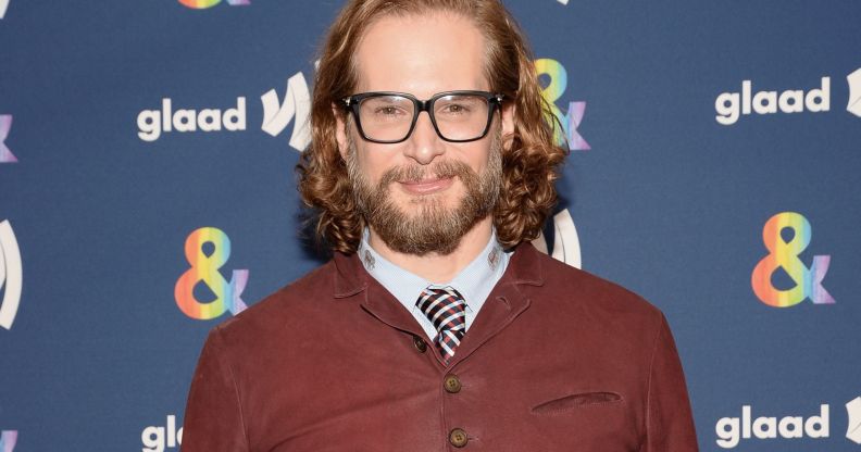 Bryan Fuller wears a white shirt, striped tie and brown jumper as he poses for a photo