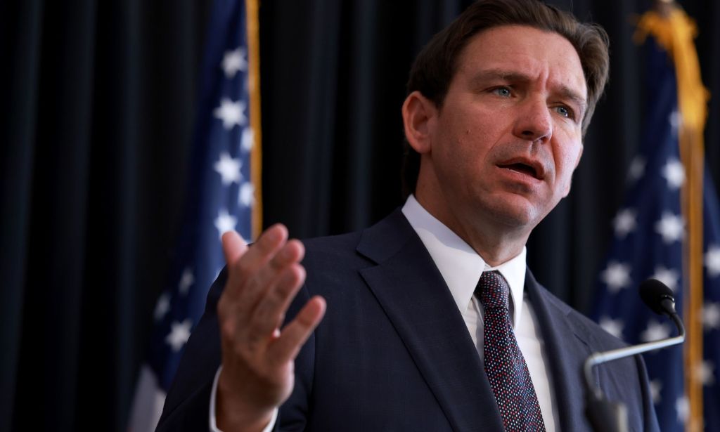 A picture of Florida governor Ron DeSantis, who championed a drag ban law in the state, wearing a suit and tie as he speaks to a crowd off camera