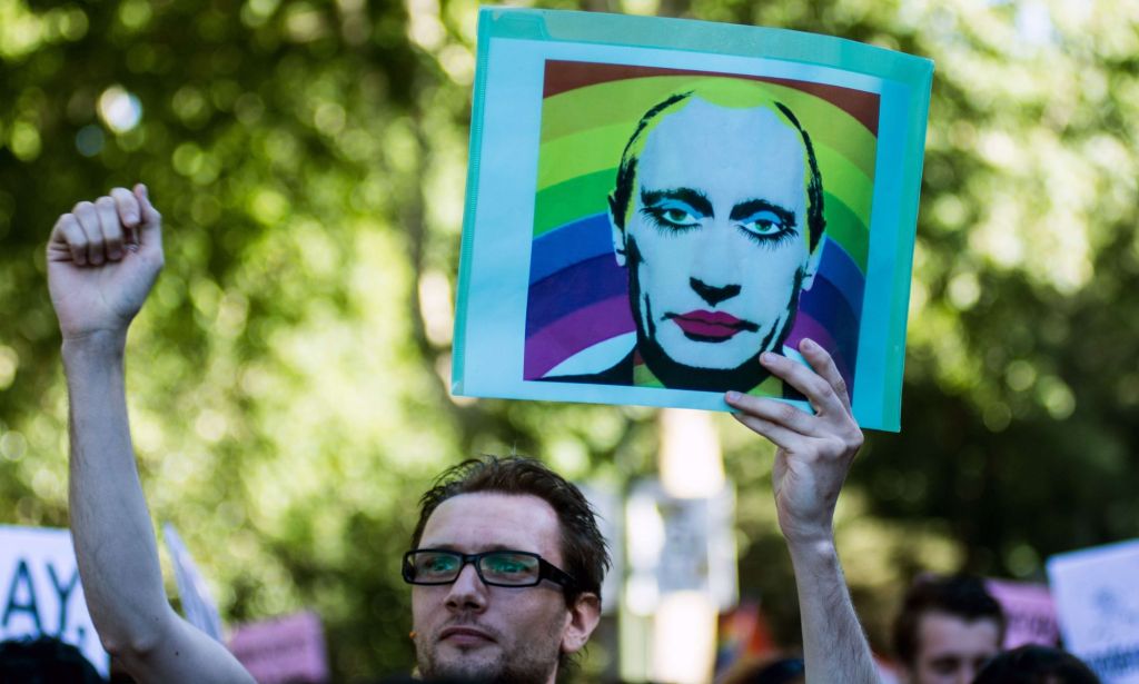 A person holds up a sign with a stylised picture of Russia's president Vladimir Putin with makeup on and a rainbow LGBTQ+ background